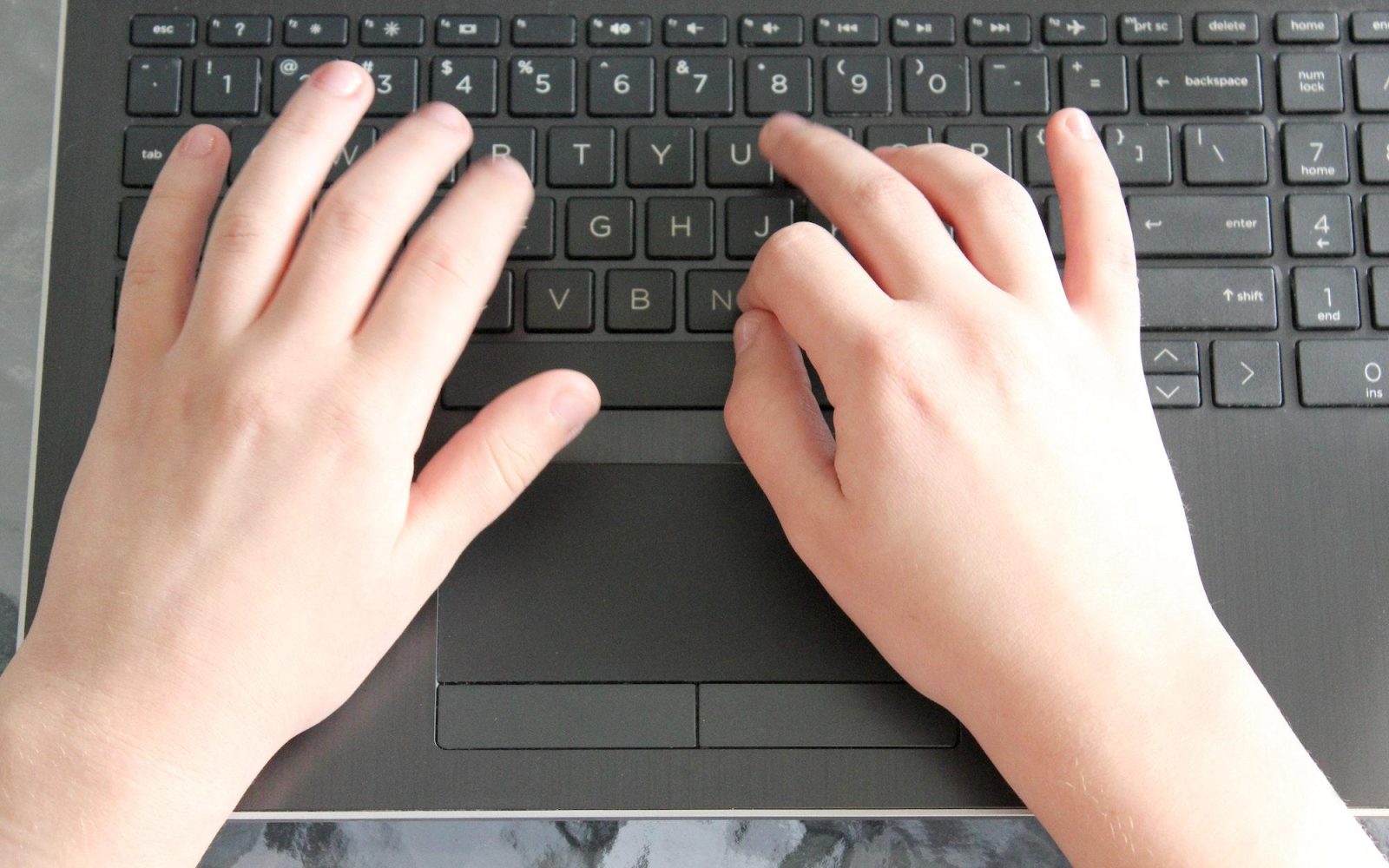 A child's hands typing away on a computer laptop keyboard