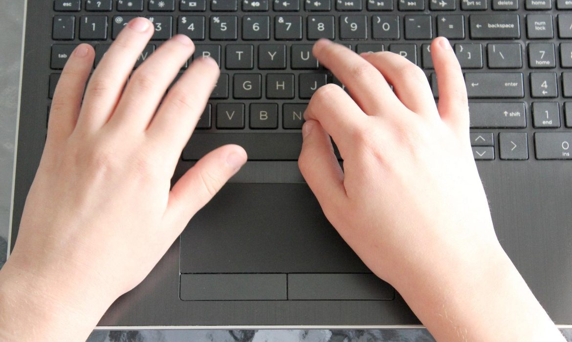 A child's hands typing away on a computer laptop keyboard